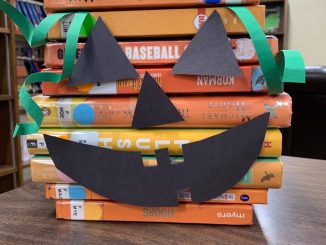 Books stacked in the library with jackolantern cut outs attached to the spines.