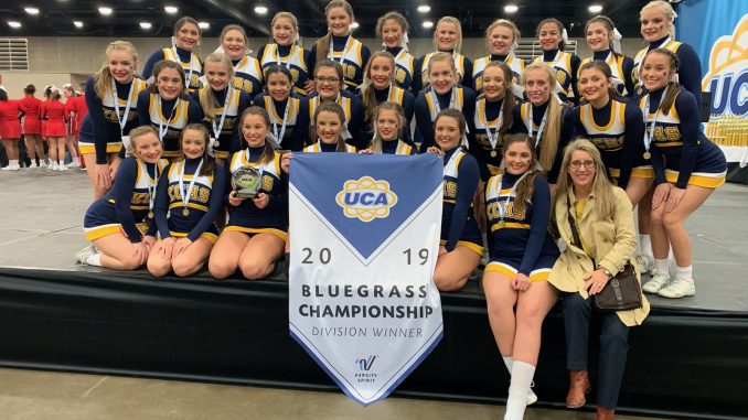 Knox Central cheerleaders shown on stage with an award winning banner from the UCA Bluegrass cheer competition.