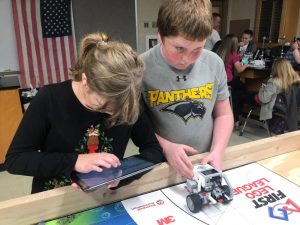 One student uses an iPad to control the robot while another sets it into motion.