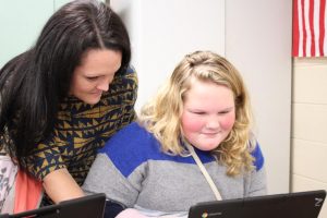 Mrs. Frederick is shown helping a student with a computer problem on a Chromebook.