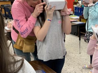 Mrs. Davis is shown adjusting the VR headset for a student.