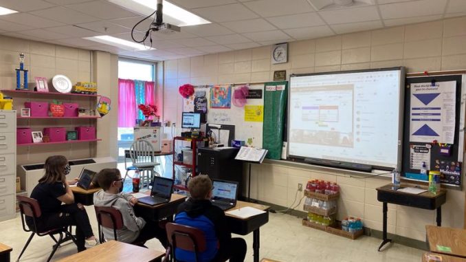 Classroom shown with students viewing teams on SmartBoard.