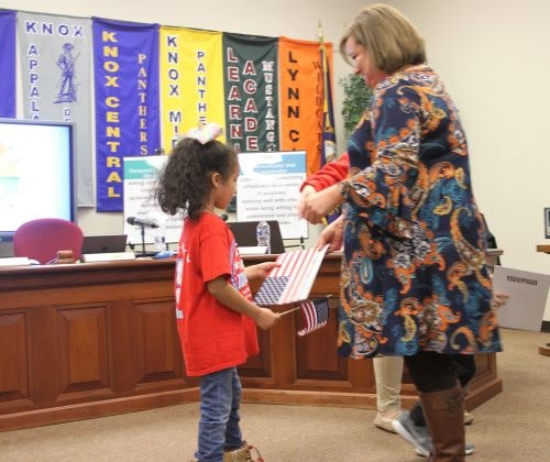 Carrie Runyon Smith shown presenting a flag to a kindergarten student 