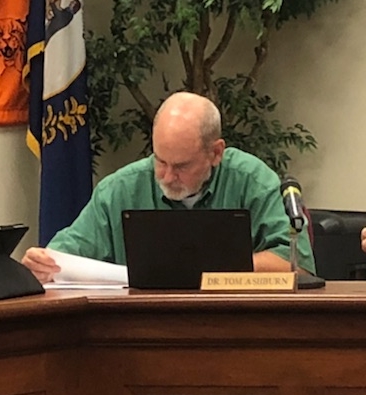 Dr. Tom Ashburn is seen studying board documents during a meeting.